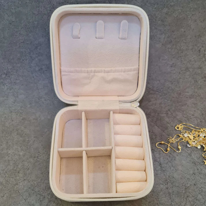 Joyero Beige abierto de frente sin joyas dentro pero en su costado derecho hay joyas sobre la mesa. Accesoriospara mujer.