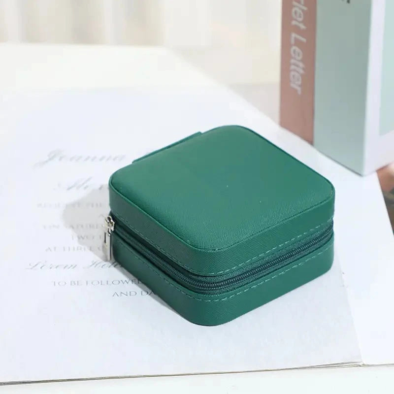 Joyero verde oscuro para guardar accesorios para mujer encima de una mesa que tiene una hoja impresa debajo.