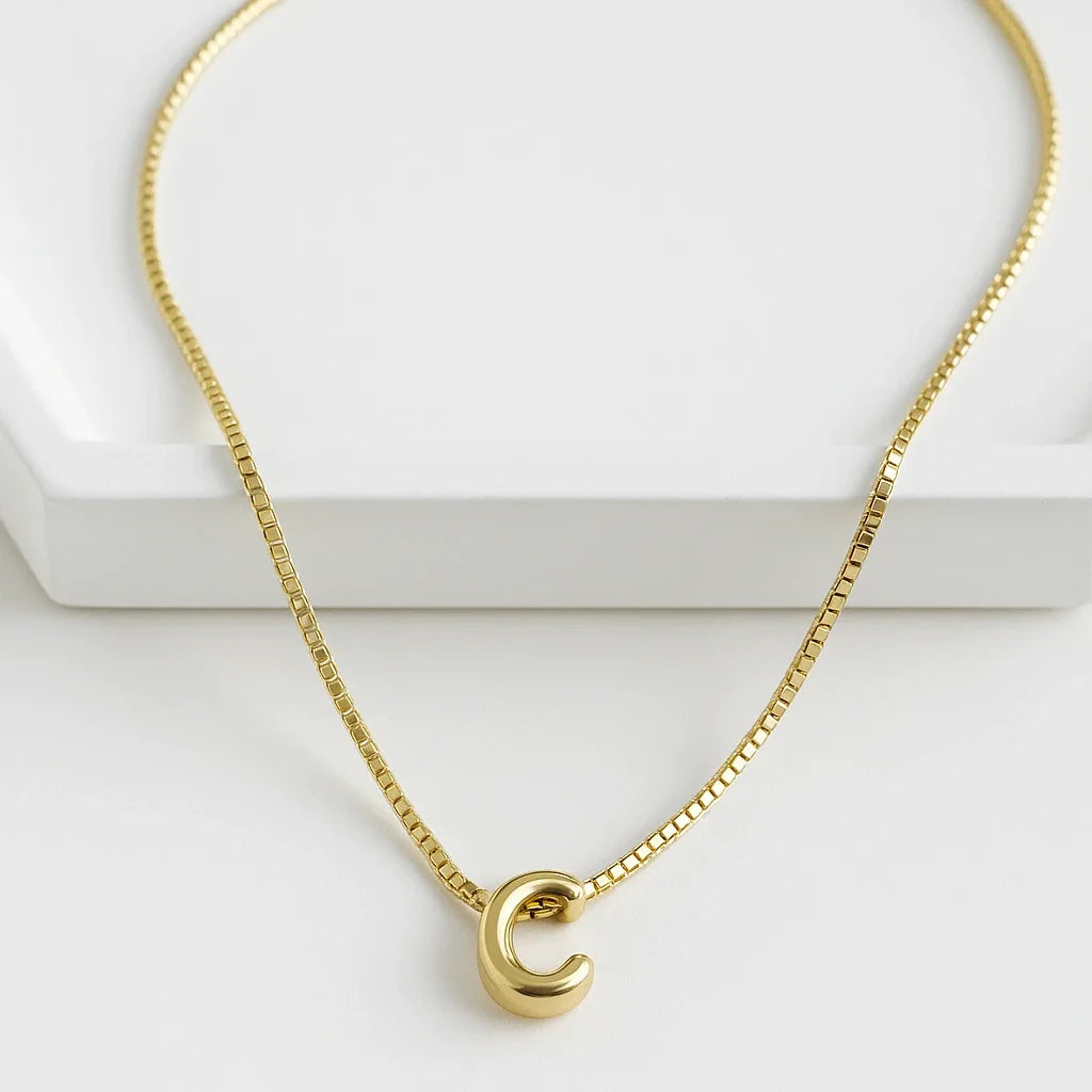 Cadena delgada con dije de letra inicial sobre fondo blanco, joya con baño de oro 24K