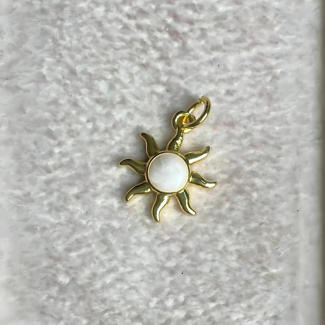 Dije de sol dorado con centro nacarado sobre tela blanca