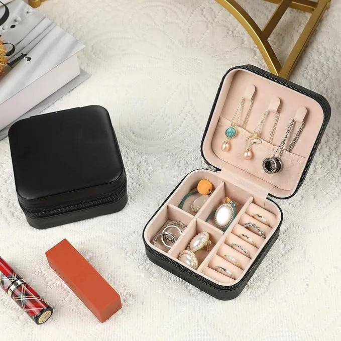 Dos joyeros negros sobre una mesa que tiene un mantel de color blanco, uno de ellos abierto con joyas y el otro cerrado. Accesorios para mujer.