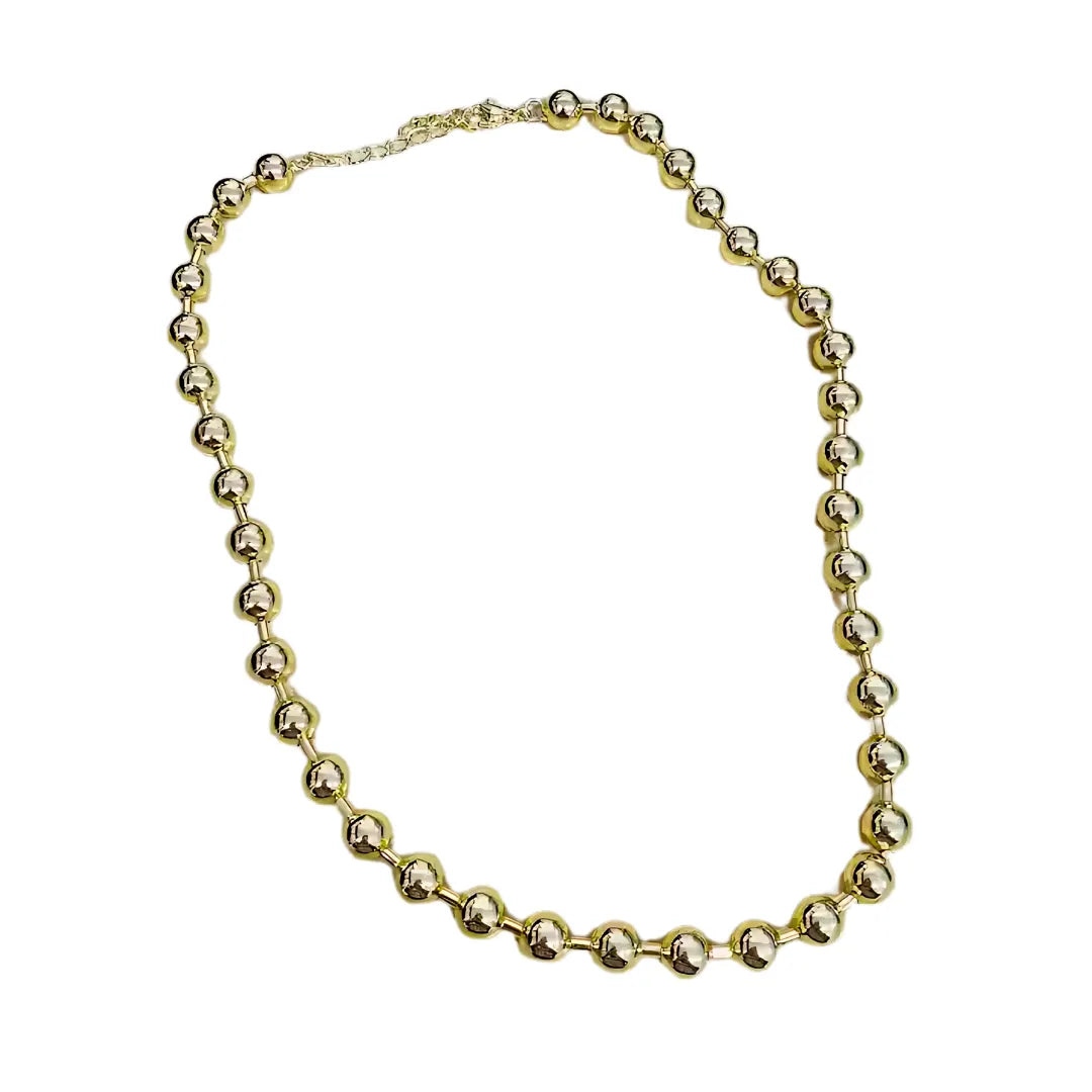 Collar con esferas medianas doradas extendido sobre superficie blanca, accesorio clásico y versátil para mujer.