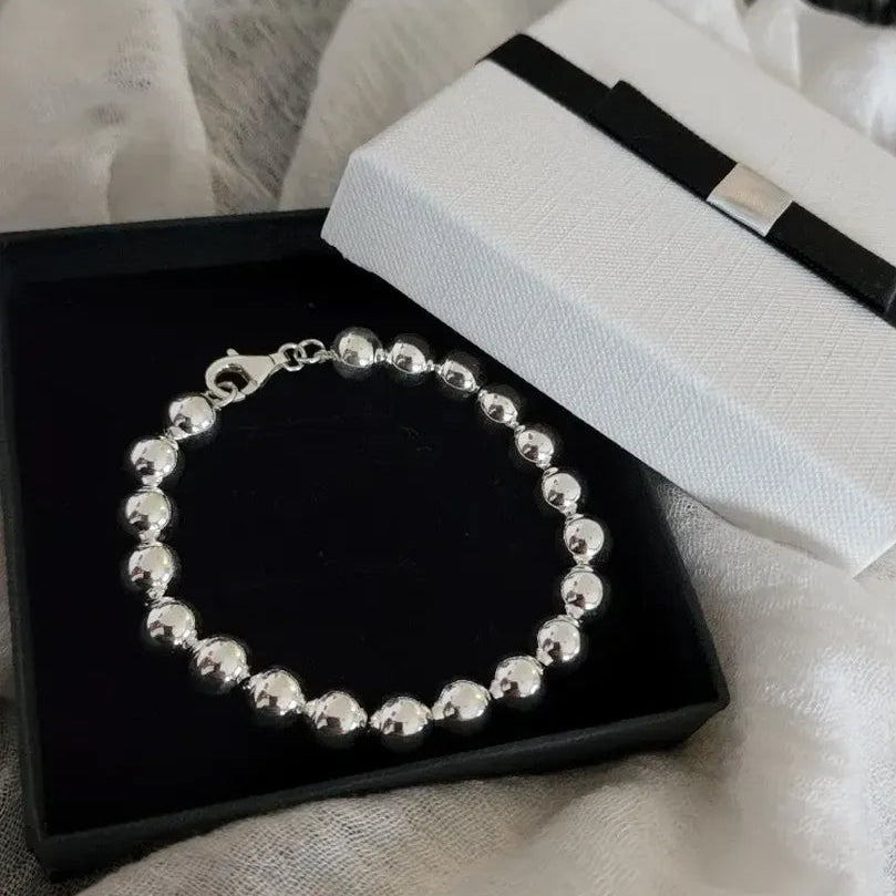 Pulsera con esferas plateadas en una caja negra con tapa blanca