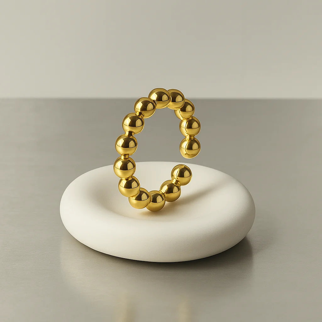 Anillo balines dorado sobre base blanca


