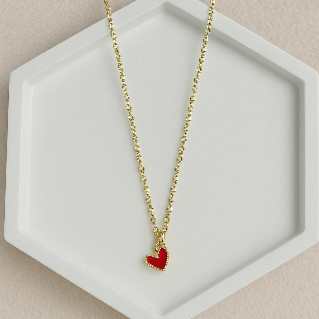 Cadena dorada con dije de corazón rojo esmaltado sobre fondo blanco

