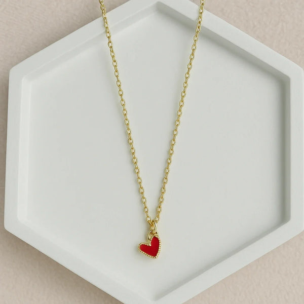 Cadena dorada con dije de corazón rojo esmaltado sobre fondo blanco
