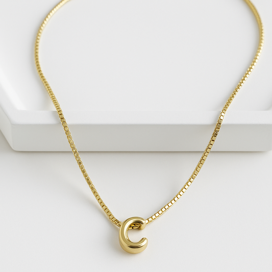 Cadena delgada con dije de letra inicial sobre fondo blanco, joya con baño de oro 24K

