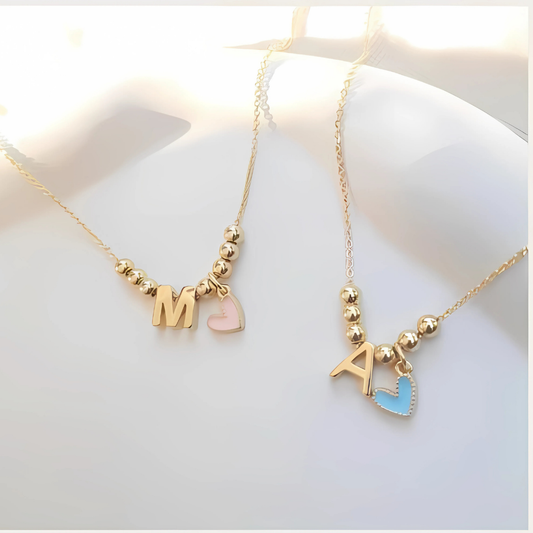 Cadenas personalizadas con letra dorada y dije en forma de corazón esmaltado sobre fondo claro

