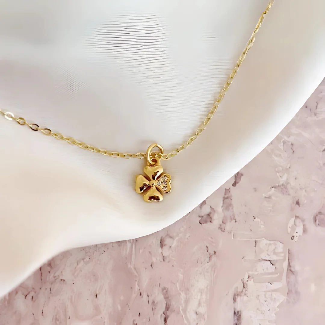Collar con dije mini trébol dorado sobre fondo satinado blanco

