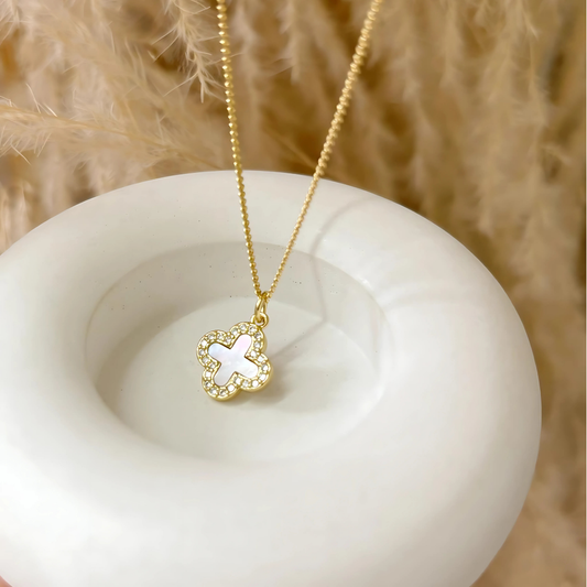 Collar dorado con dije de trébol blanco tornasol sobre fondo neutro para mujer

