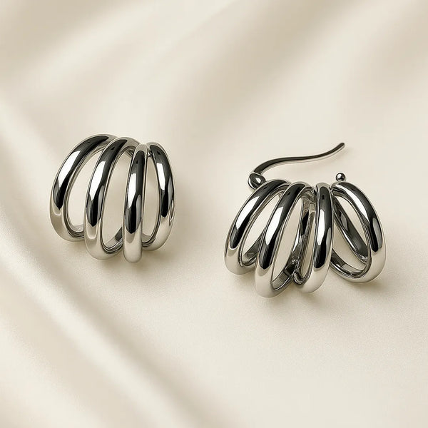 Aretes plateados modernos tipo resorte con acabado espejo sobre fondo beige – accesorios para mujer con diseño original