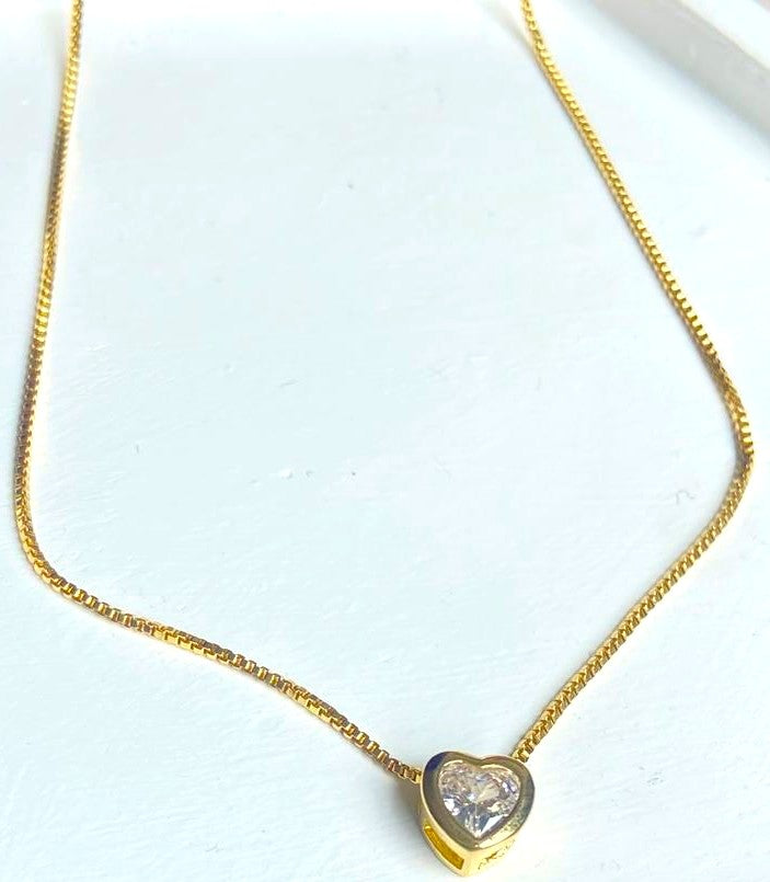 Collar dorado con dije de corazón de cristal brillante sobre fondo blanco

