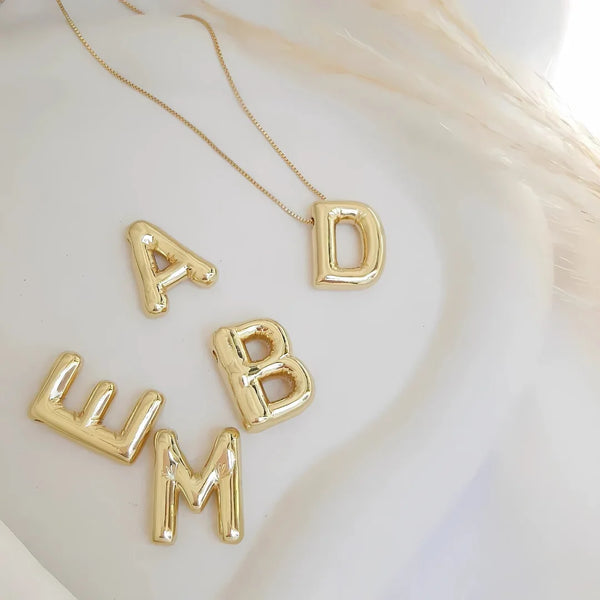 Collares dorados con dijes de letras grandes personalizadas sobre fondo blanco
