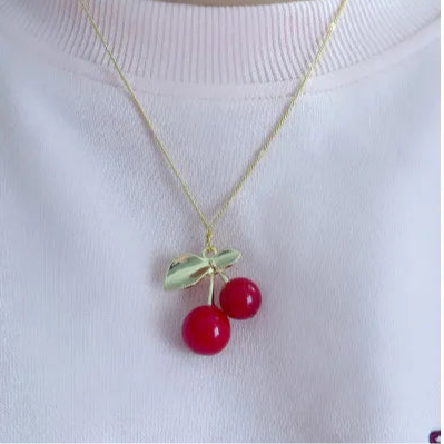 Detalle del dije de cereza en dorado y rojo con cadena fina

