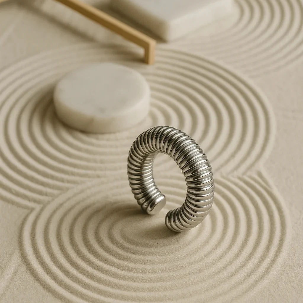 Accesorio ear cuff plateado rodinado sobre arena blanca zen en forma vertical
