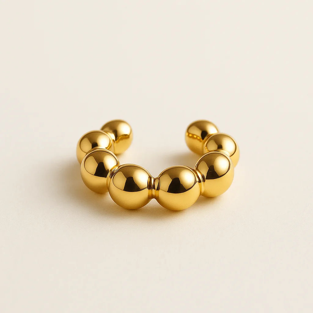 Ear cuff dorado con diseño de balines sobre fondo beige

