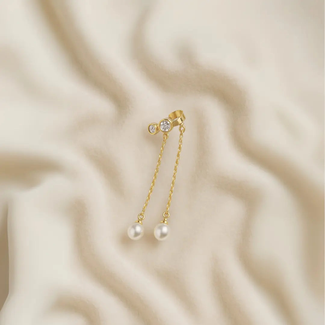 Ear cuff con cristales y perlas colgantes sobre fondo beige texturizado

