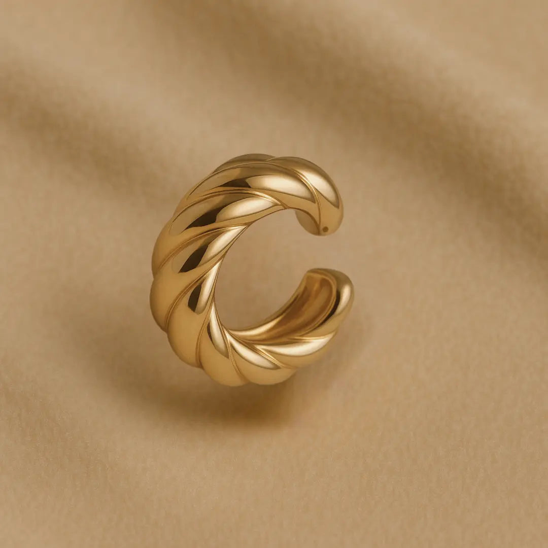 Ear cuff dorado tipo trenza en fondo neutro elegante


