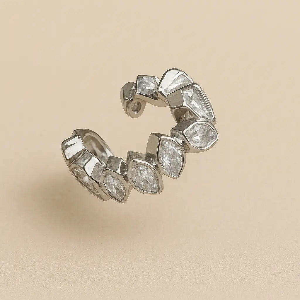 Ear cuff plateado con hojas y circones sobre fondo beige

