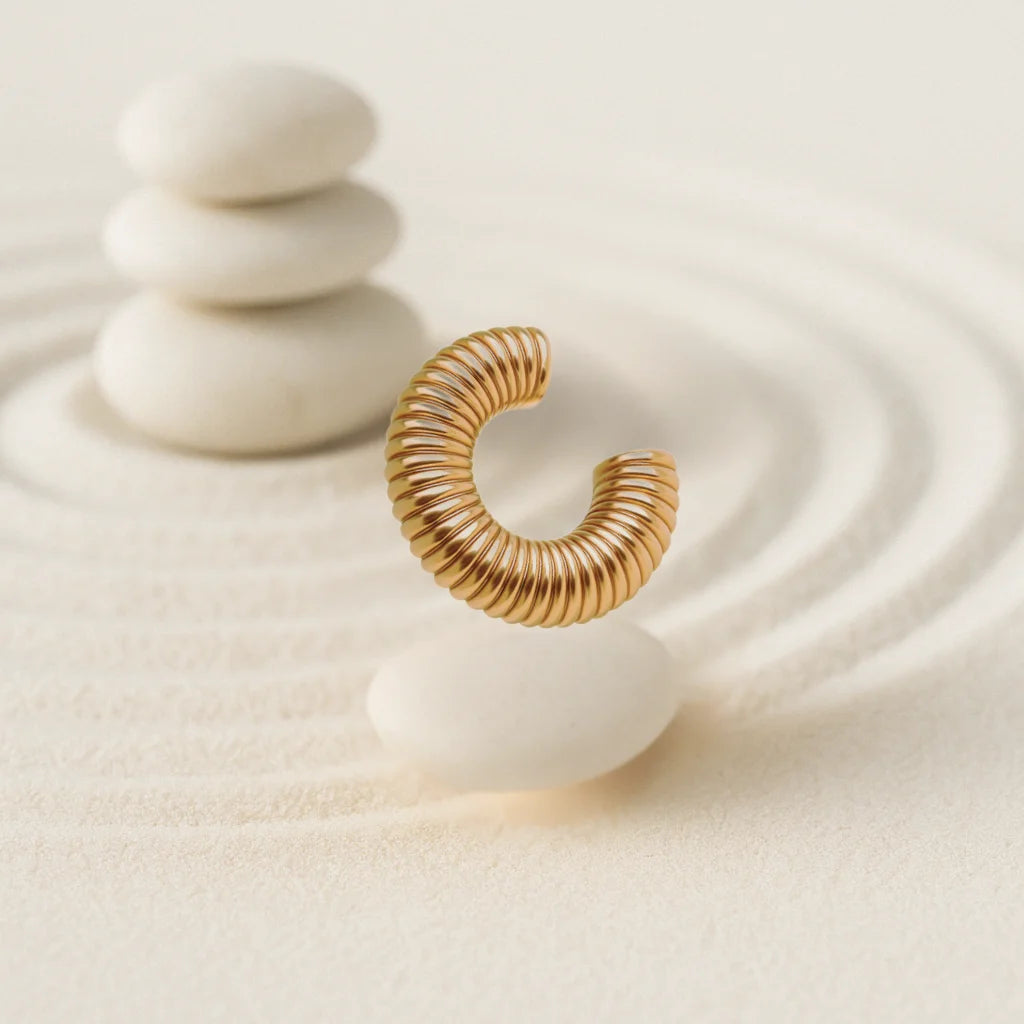 Ear cuff dorado con textura de rayas sobre base blanca

