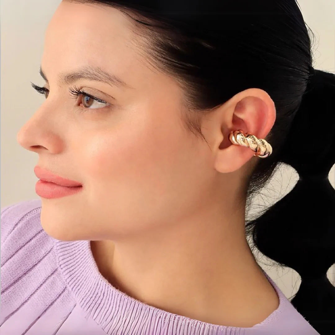 Ear cuff trenzado dorado colocado en la oreja de una mujer

