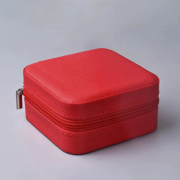 Joyero rojo cuero texturizado cerrado sobre un fondo gris claro, accesorios para mujer.