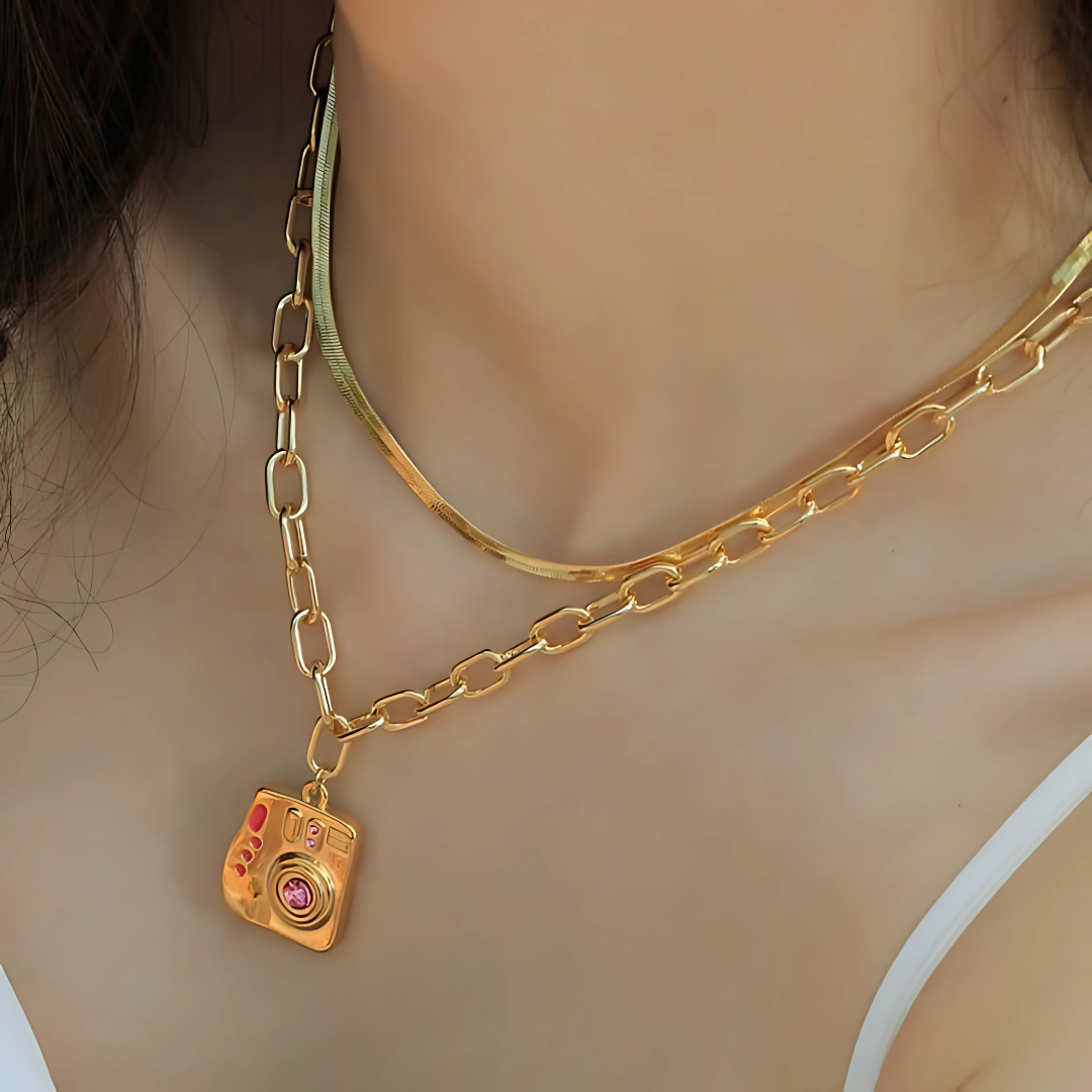 Accesorio femenino con simbolismo emotivo y diseño creativo. Joya dorada con piedra central rosa para amantes de la fotografía


