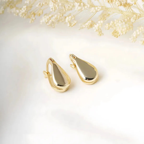 Aretes dorados topo gota baby sobre fondo beige, accesorios para mujer elegantes y delicados.